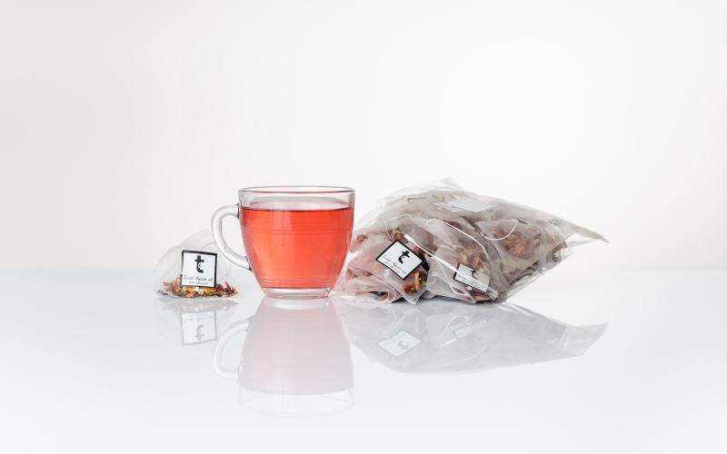 A cup of brewed Easter Tea sitting next to Easter Tea pyramid teabags