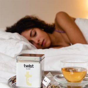 A woman in bed drifting off into a good quality sleep, with a Twist Teas caddy in the foreground.