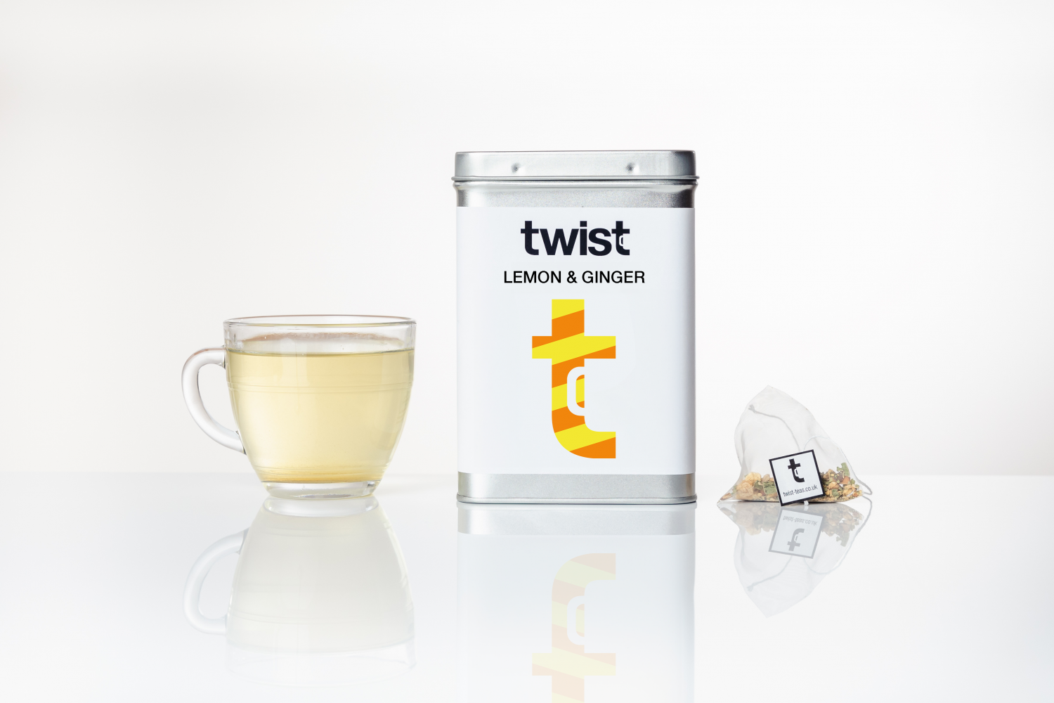 A lemon and ginger caddy personally positioned in between a brewed tea and a Twist Teas tea bag.