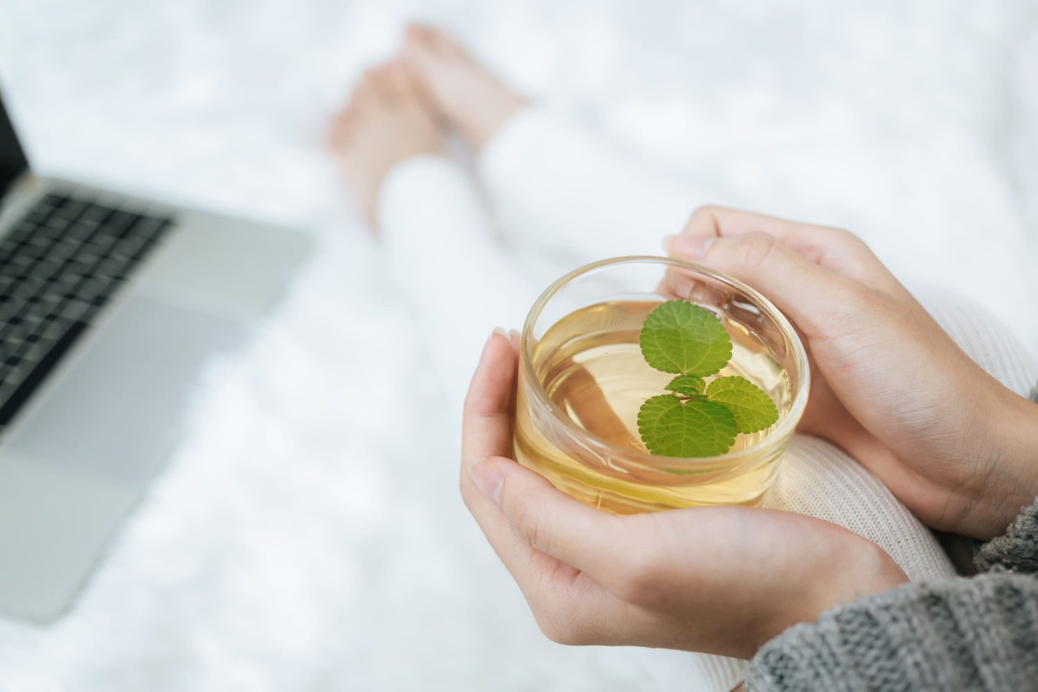 Two hands nursing a cup of freshly brewed top quality green tea.