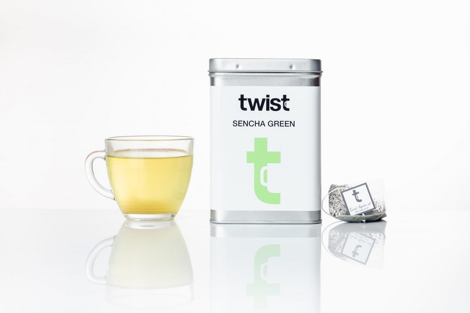 A Twist Teas 'Sencha Green' caddy placed in between a quality cup of green tea and a teabag.