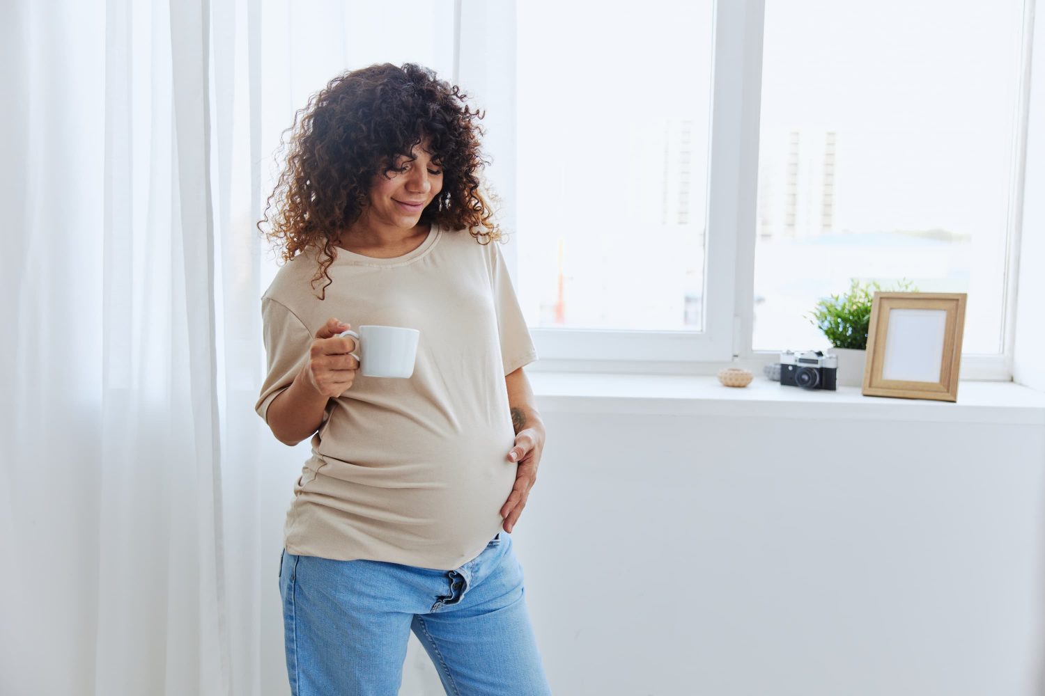 A view of a pregnant woman standing and drinking tea to give her a better experience with her pregnancy.